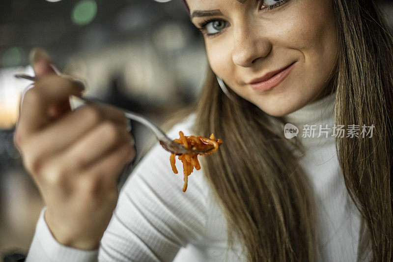 ． 意大利面条。一个有趣的有吸引力的年轻女子在餐厅吃意大利面。一个饥饿的女人在吃美味的意大利面。